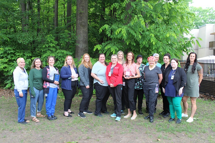 A group of 16 female medical staff outside with trees. Some hold plaques.