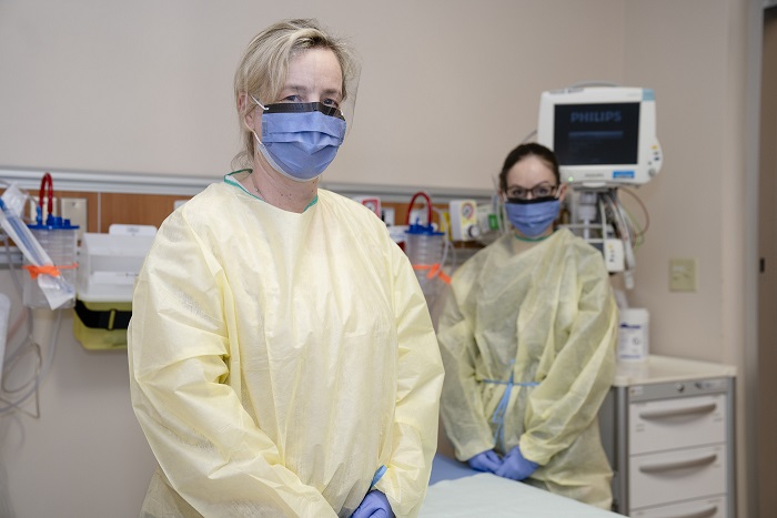 Two tired looking nurses in gowns and wearing masks.