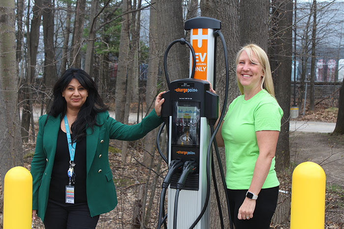 Two women standing outside beside an EV Charging station.