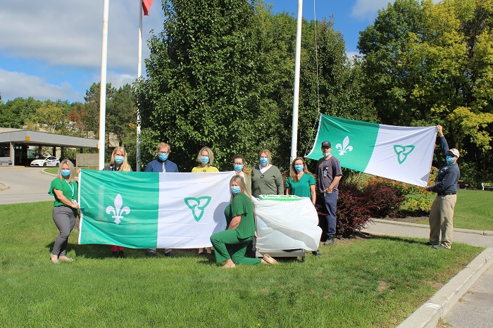 Ten people holding up 2 oversized Franco-Ontario flags.