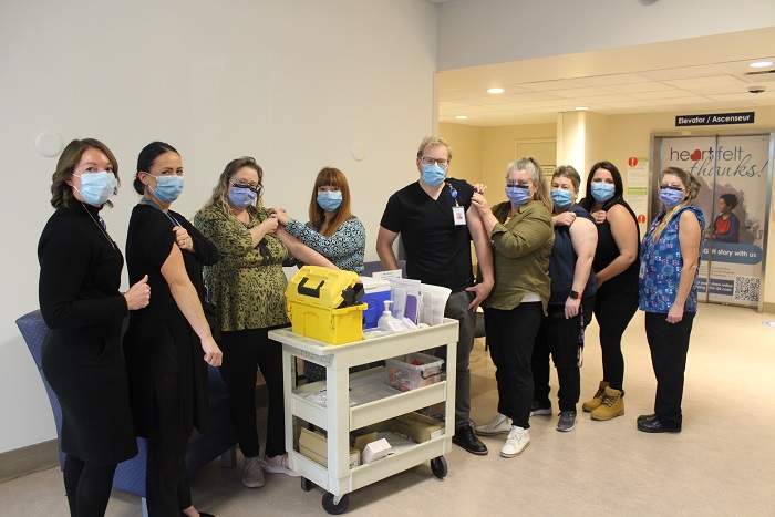 Nine people in masks getting ready to receive their flu shot.