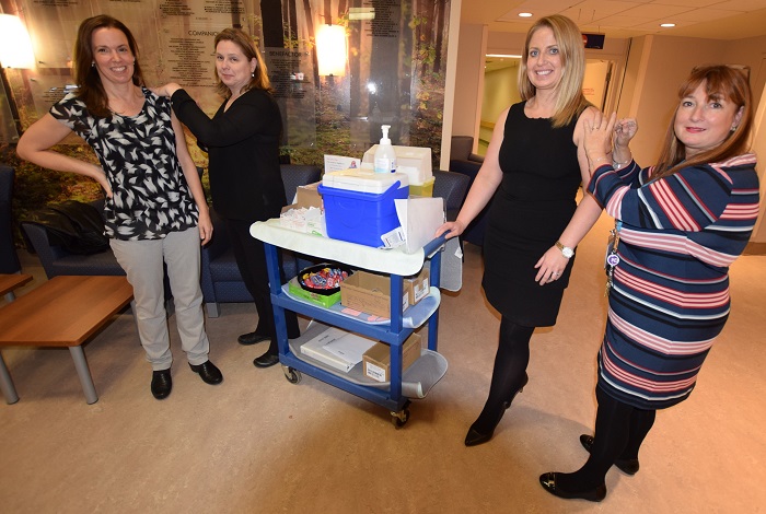 Four women pose around a rolling table that has a blue cooler and various medical supplies on it.