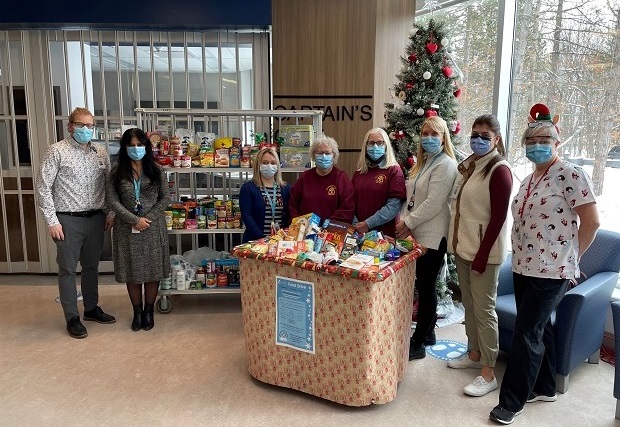 Eight volunteers pose with a metal shelving unit and a huge hamper full of food for the food drive.