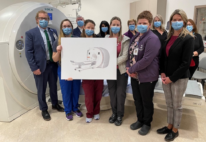 A group of 11 people posing with a large poster of an MRI machine