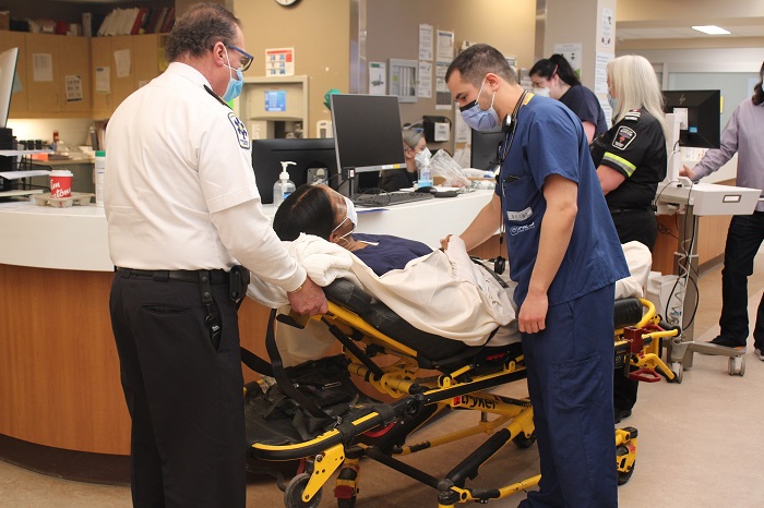 Ambulance attendant and a medical staff team member wheel in a woman on a stretcher.