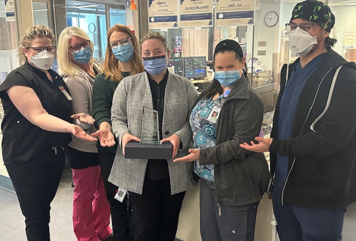 5 women and a man all in masks posing with a trophy in the ER area of the hospital.