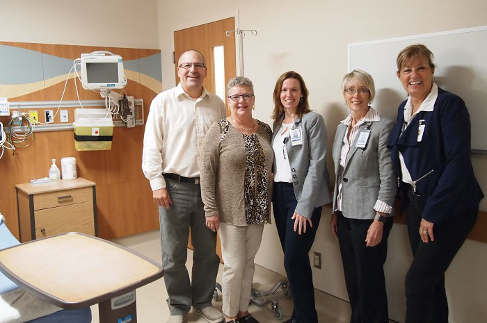 A group of 5 people gather for a photo inside an inpatient room. Three of them are wearing badges