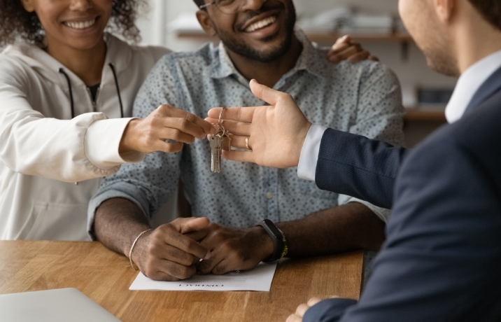 A man handing over some keys to a smiling couple.