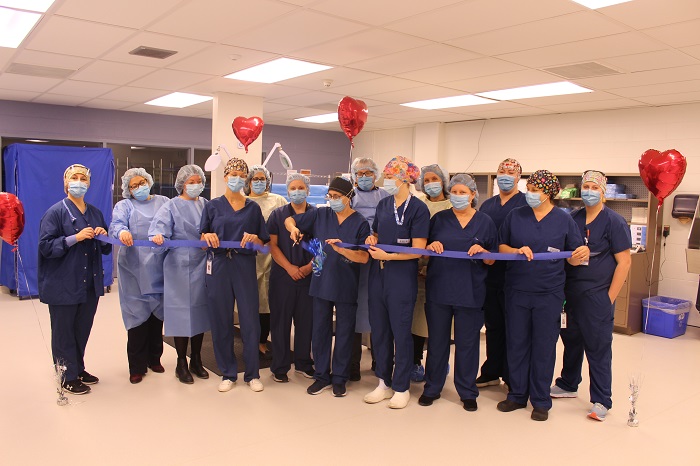 14 Medical workers pose with a blue ribbon. The person in the centre is cutting the ribbon.