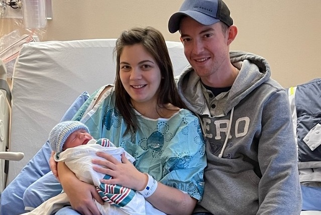 A young couple sitting on a hospital bed holding a brand new baby boy.