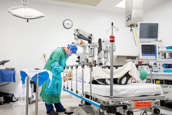 A patient in a bed with large white machines above him. A male doctor is attending to the patient.