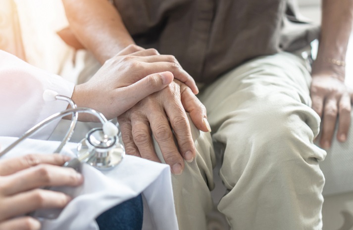 A medical staff with a hand over a patient's hand as they sit together.