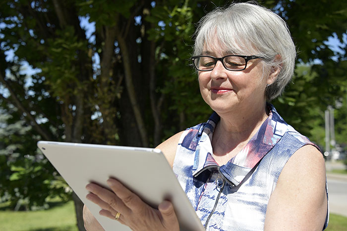 Grey haired women wearing black glasses looking at a tablet