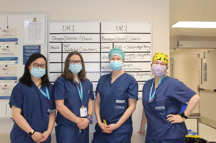 Four surgeons in dark blue scrubs pose outside the operation desk.