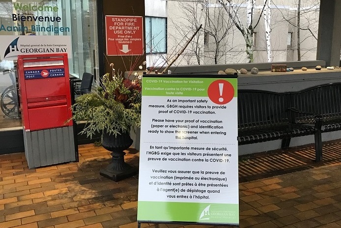 The hospital front entrance showing a mail box and a sign describing COVID-19 restrictions