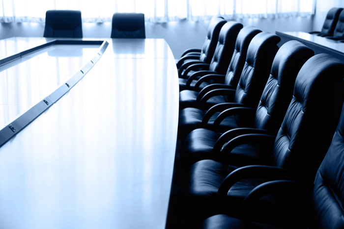 An empty board room with a shiny table and black leather chairs.